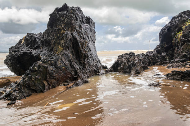 Black dark boulders lying on a beach after the coast in Axim Ghana West Africa