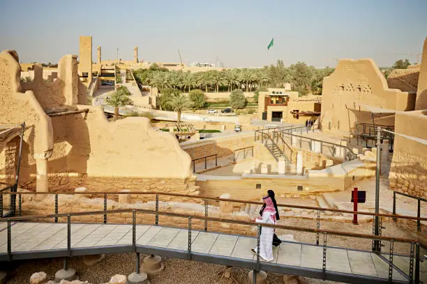 Full length side view of Middle Eastern couple in traditional attire walking together across footbridge at UNESCO World Heritage Site near Riyadh. Property release attached.