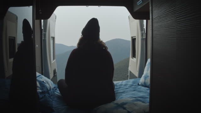 Woman sit down in the bed of a motor home looking the views.
