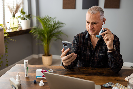 Mature man consulting with his doctor online on his phone, using a pump during an asthma attack