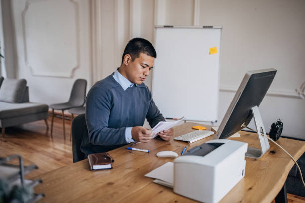 istock Business man sitting at the desk and working on computer while looking at some documents 1391378950