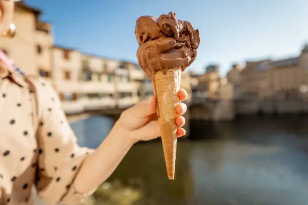 Holding chocolate ice cream in a waffle cone on background of the Old bridge in Florence, Italy. Concept of italian gastronomy and landmarks