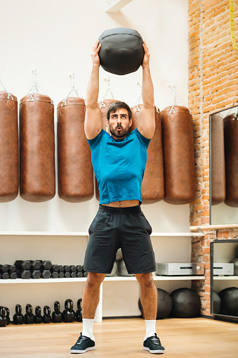 Fit muscular man working out with a Pilates Medicine Ball raising it above his head. Often used for neuromuscular rehabilitation
