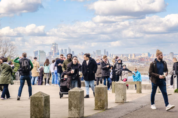 London, United Kingdom - April, 09 2022: Diverse group of tourists at Greenwich Park in London with a view north westwards over the London skyline.