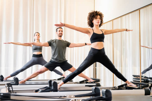 clase de pilates de personas diversas haciendo posturas de yoga de pie - pilates fotografías e imágenes de stock