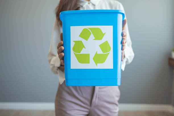 Young Asian woman with a crate for recycling. A woman collecting and separating recyclable garbage into a trash bin at home. A woman collecting garbage and holding a recycle bin