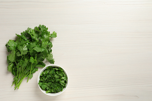 Fresh green cilantro on white wooden table, flat lay. Space for text