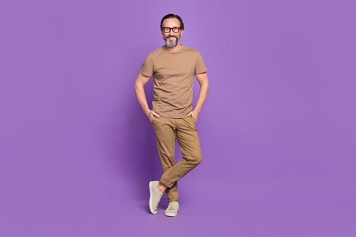 Full length photo of mature cheerful man hands in pocket wear modern clothes isolated over violet color background.