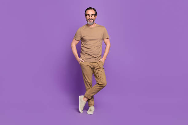 Full length photo of mature cheerful man hands in pocket wear modern clothes isolated over violet color background stock photo