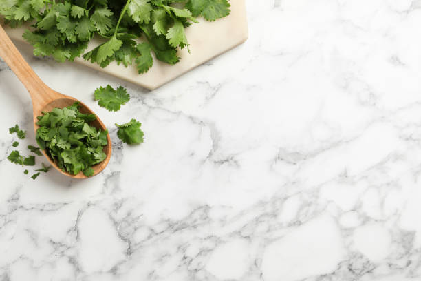 istock Fresh green cilantro and wooden spoon on white marble table, flat lay. Space for text 1391395233