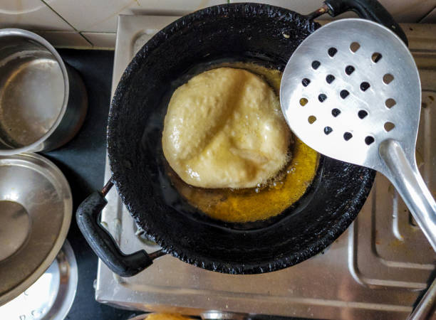 Stock photo of deep fried puri, women frying wheat flour puri or bhatura until its get golden brown color in cooking oil. Picture capture in Indian kitchen area at Bangalore,Karnataka, India. stock photo