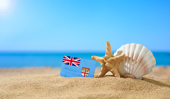 Tropical beach with seashells and Fiji flag. The concept of a paradise vacation on the beaches of Fiji.