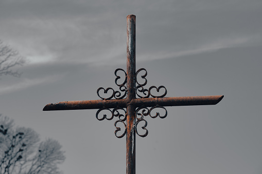 Old weathered metal cross at the graveyard against dark sky. Old cemetery. Mystical Halloween background with copy space. Selective focus