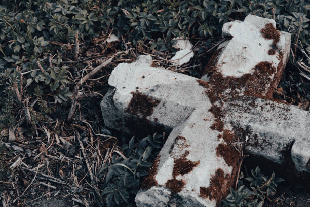 Halloween background with copy space. Toppled stone crucifix on the ground. Abandoned ancient cemetery with broken gravestone. Mystery halloween concept, old churchyard
