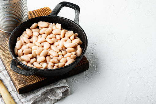 White canned beans set, with metal can, in cast iron frying pan, on white stone  surface, with copy space for text