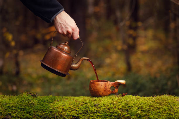 Man pours delicious coffee from vintage kettle into wooden cup on mossy old tree. stock photo