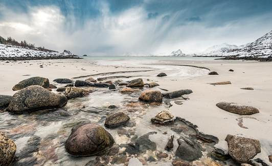 Snowy winter landscape at the shore of on of the islands of the Lofoten archipel near Heamingsvear in Norway The mountains are covered in snow and there is ice floating on the water.