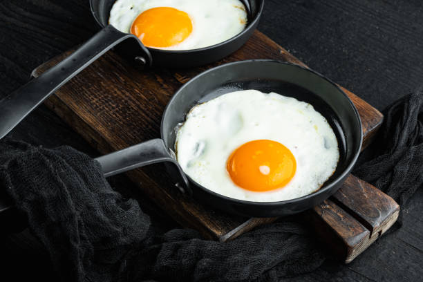 istock Fried eggs with cherry tomatoe and bread for breakfast in cast iron frying pan, on black wooden table background 1391406401