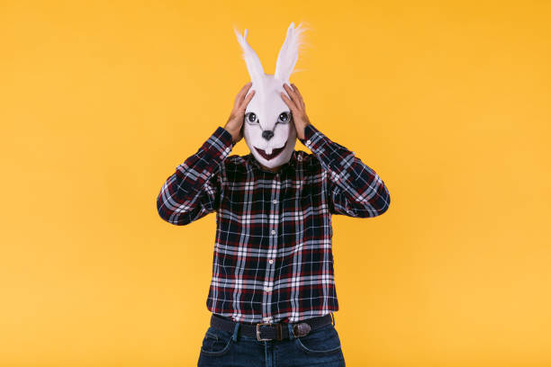 disgusted person wearing rabbit mask wearing checkered shirt and jeans, putting hands to head disgruntled, on yellow background. carnival, party, easter and celebration concept. - mask religious celebration horizontal easter imagens e fotografias de stock