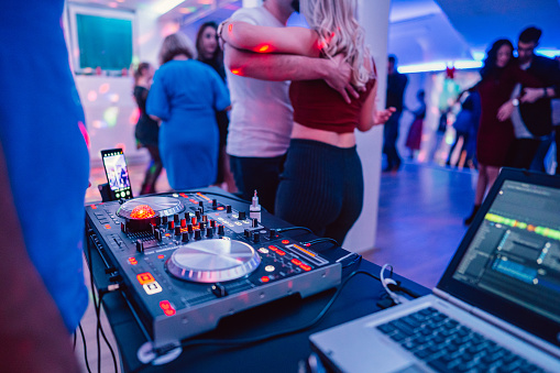 A close-up of a DJ playing and mixing music for a salsa party indoors.