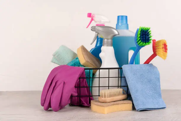 Photo of Basket with cleaning products against light wall background with copy space. Cleaning service concept. Detergents and household chemicals. Copy space