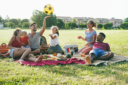 Happy families having fun doing picnic at park outdoor in summer vacation - Focus on right mother face
