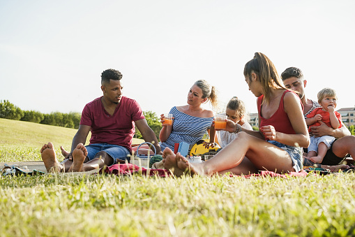 Happy families having fun doing picnic at park outdoor in summer vacation - Focus on center woman face