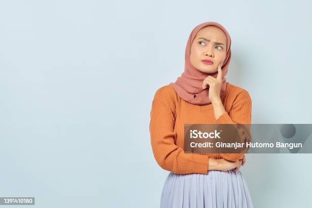 Portrait Of Beautiful Young Asian Muslim Woman In Brown Sweater Looking Serious Thinking About Question And Looking At Copy Space Isolated On White Background Muslim Lifestyle Concept Stock Photo - Download Image Now