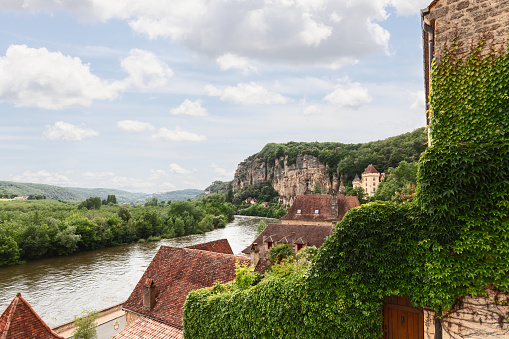 High rocky banks of full-flowing Dordogne river covered with dense forest and most beautiful villages of France nestled on its slopes. New Aquitaine region, France