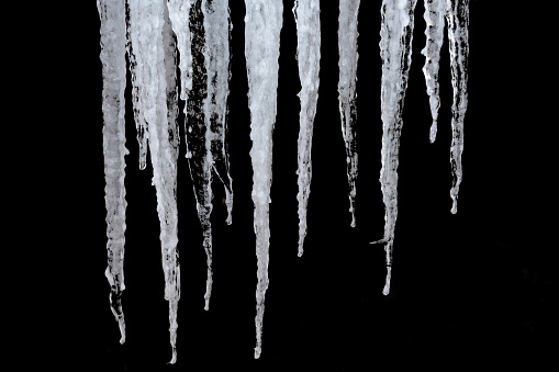 In spring, transparent icicles of different lengths and widths hang from the roof. close-up. Textured black background. The beauty of nature in the smallest detail