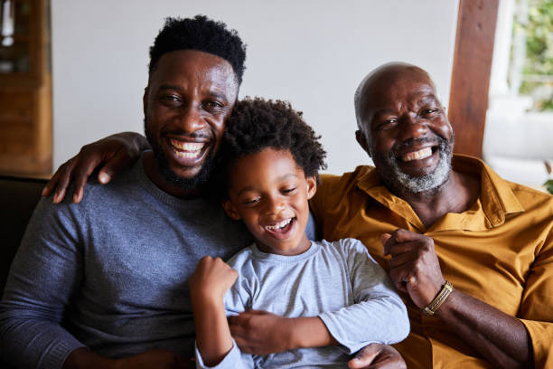 Man and his senior dad and young son laughing together on a sofa stock photo