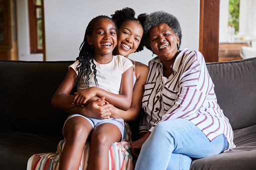 Portrait of an African woman and her senior mother and young daughter laughing while sitting on a sofa in their living room at home