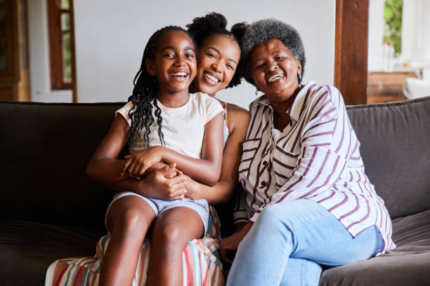 Woman and her senior mom and young daughter laughing while sitting at home Portrait of an African woman and her senior mother and young daughter laughing while sitting on a sofa in their living room at home black african girls pictures stock pictures, royalty-free photos & images