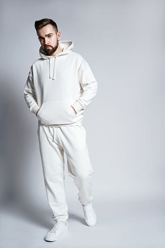 Handsome man wearing blank white hoodie and pants posing on gray background