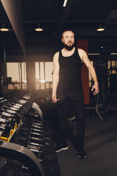 istock A young man with a beard is posing in the gym with dumbbells. 1391426083