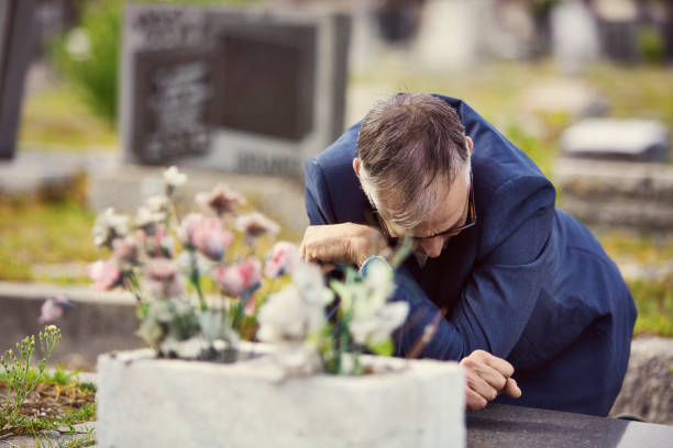 Man kneels in front of a grave in a cemetery