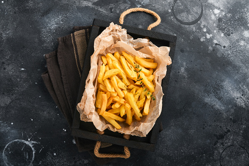 French fries. Tasty French fries server on parchment paper on wooden cutting board with tomato and cheese sauce on old black  background. Diverse Keto Dishes. Fast food and unhealthy food concept.