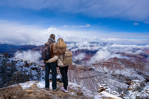Man and woman  standing on top of the mountain enjoying beautiful winter landscape. People standing on the mountain cliff. Grand Canyon National Park, Arizona, USA.