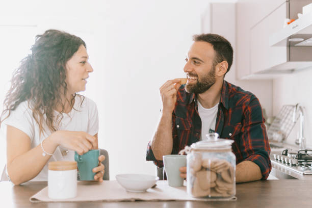 istock Engaged couple has breakfast together in their new home - young couple smiling while drinking and eating in the kitchen - warm filter on background 1391433093