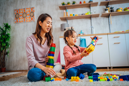 Mother and daughter playing together with colorful construction toys on a carpet on the floor at home