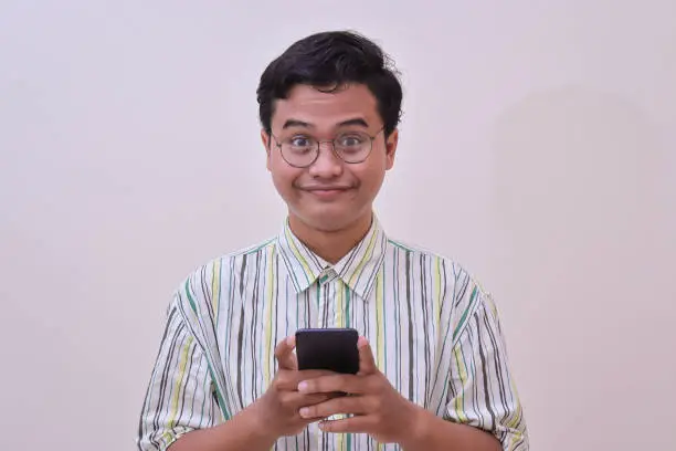 Photo of funny Asian man holding a mobile phone with two hands