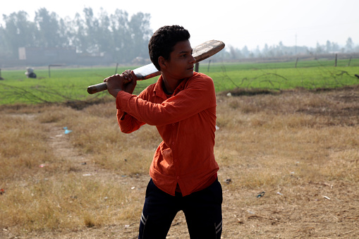 Rural boy playing cricket in village located in Haryana, India.