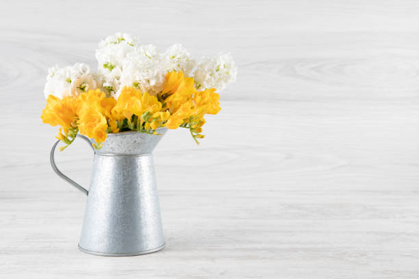 Flowers in a vase on rustic wooden table. Blank space for text on the wall
