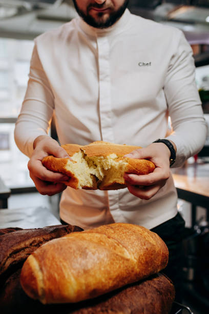 istock Handsome baker in uniform breaks freshly baked bread at the bakery 1391451314