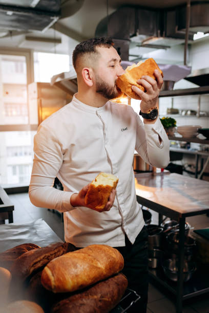 istock Handsome baker in uniform biting freshly baked bread at the bakery 1391451332