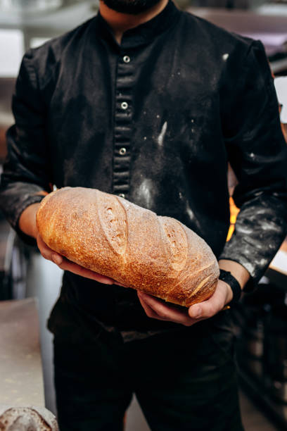 istock Handsome baker in uniform holding freshly baked bread at the bakery 1391451842