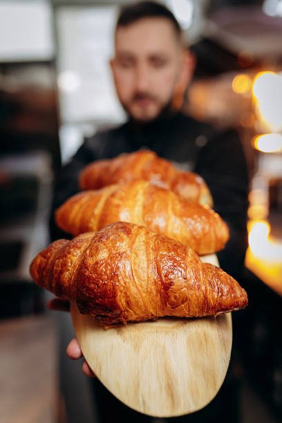 istock Handsome baker in uniform holding freshly baked croissants at the bakery 1391452129