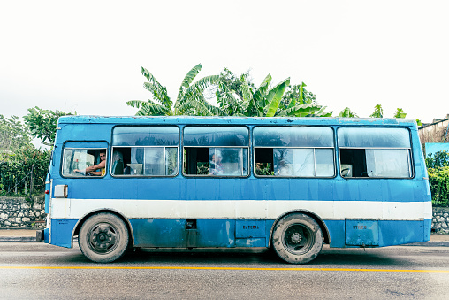 Santa Clara, Villa Clara, Cuba - November 7, 2019: A man drives an obsolete Giron bus on a wet pavement. The scene is taken on a rainy and overcast weather in the Central Road which is one of the main streets in the provincial capital city.