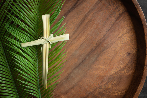 Border of cross made from dried palm leaf laying on a palm branch on a teak wood tray with copy space shot from above