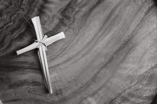 Simple cross made of dried palm leaf on a teak wood background with copy space